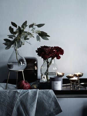 Ihastele tänä jouluna perinteisen joulutähden sijaan tummia, viininpunaisia neilikoita ja krysanteemeja. Kaunis asetelma syntyy, kun lisäät  mukaan samasta sävymaailmasta granaattiomenan ja viikunan.  Julia-maljakolla  on pyöreä pohja ja metallinen jalusta, 29,90 e, Indiska.  Oyster-tuoksukynttilä  on tyylikkäässä 1970-lukua henkivässä, tummassa purkissa, 197 e, Kartell. Muuton  Silent-maljakko  35 e ja Gauharin  Tranquility-tuoksukynttilä  38 e, Formverk.  Asala-tuikkuteline  44,90 e, Indiska, ja  tarjoiluvaunu  290 e, Moko. Pellavaliina kuvausrekvisiittaa.