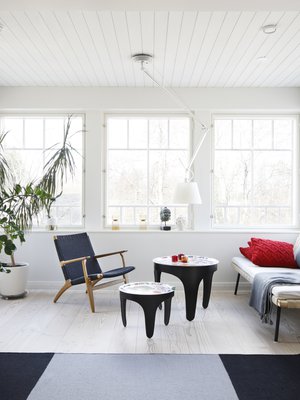 Olohuoneen lasiverantamaisessa syvennyksessä istutaan kahvilla. Viherkasvien välistä aukeaa ovet terassille. Svenskt Tennin tarjotinpöydät ovat Tukholmasta. Sohvana toimii vielä toistaiseksi Ikean daybed, kunnes se muuttaa alakertaan valmistuvaan oleskelutilaan. Kevyt nojatuoli on Hans J. Wegnerin, matto Valannin.