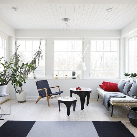 Olohuoneen lasiverantamaisessa syvennyksessä istutaan kahvilla. Viherkasvien välistä aukeaa ovet terassille. Svenskt Tennin tarjotinpöydät ovat Tukholmasta. Sohvana toimii vielä toistaiseksi Ikean daybed, kunnes se muuttaa alakertaan valmistuvaan oleskelutilaan. Kevyt nojatuoli on Hans J. Wegnerin, matto Valannin.