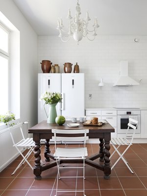 Keittiön barokkipöytä on tuotu Belgiasta, kuten kattokruunukin. Bistrotuolit palvelivat vuosia mökillä ja siirtyivät kotiin, kun mökki myytiin. Lattialla on Pukkilan Litocer-laattaa.