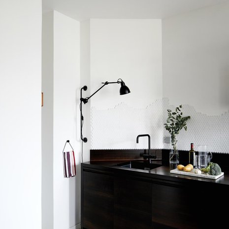 Keittiön allastason ylle Kati ei halunnut yläkaappeja vaan ilmavuutta. Koska seinä on kulmikas, tuntui vapaasti aaltoileva laatoitus sopivalta idealta. Kun kukaan rakennusmiehistä ei ymmärtänyt Katin suunnitelmaa, hän laatoitti seinän itse Pukkilan mattavalkoisilla HX-90 Hexagon -laatoilla. Hana on Tapwellin, ja työtason valaisee Lampe Grasin numero 210.