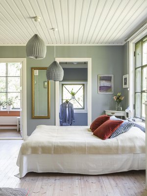 Makuuhuoneen seinien värisävy on rauhoittava salvianvihreä. Sängyn päällä on Tipukonvehtin villapeite. Tyynyt ovat Mokosta ja valaisimet Habitatin. Kulmapöytä on löytö kirpputorilta. Koska talossa ei ollut vaatekaappeja, makuuhuoneen perälle päätettiin rakentaa vaatehuone.