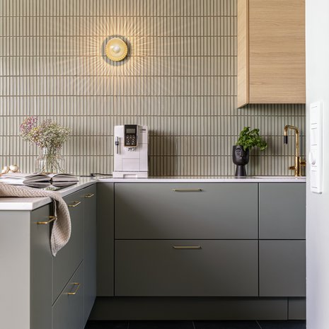  Nuuran seinävalaisin luo päällä ollessaan seinälle valon ja varjojen taideteoksen. Helppohoitoisuuden vuoksi keittiöön valittiin kvartsikomposiittitaso, Okite Calacatta Bettogli, Edelstein Special. Nixi-keittiön vaalean tammen sävyiset yläkaapit ovat mallia Heta ja alakaapit ovimallia Mira sävyssä Huurre varpu.