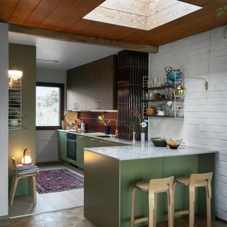 Niemekettä valaisee kattoikkuna, jonka alla oli alun perin ruokapöydän paikka. Niemekkeessä on kaappitilaa sekä keittiön että olohuoneen puolella. Liesituuletin on piilossa yläkaapissa. Yläkaappien ovet ovat täyspuuta, ne on valmistanut Mittapuu. Kalkkikivitaso on Tuliven Jura Grey.