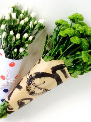 Porkkanaleimattu paperi sai sis&auml;&auml;ns&auml; neilikoita ja ymp&auml;rilleen pilkullista nauhaa, graafisilla kuvioilla koristeltu voimapaperi t&auml;ydentyi mustavalkoisella pakkauslangalla ja raikkailla vihreill&auml; krysanteemeill&auml;.