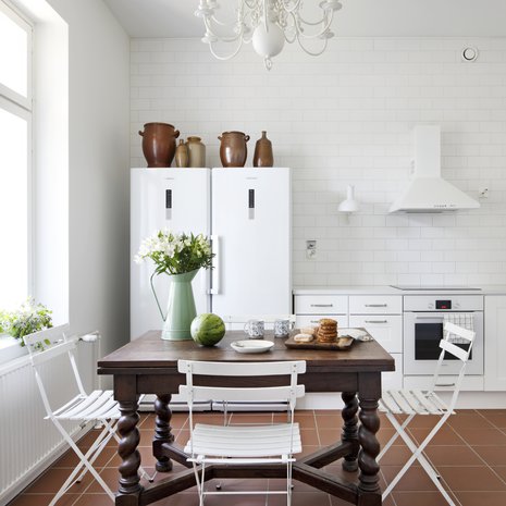 Keittiön barokkipöytä on tuotu Belgiasta, kuten kattokruunukin. Bistrotuolit palvelivat vuosia mökillä ja siirtyivät kotiin, kun mökki myytiin. Lattialla on Pukkilan Litocer-laattaa.