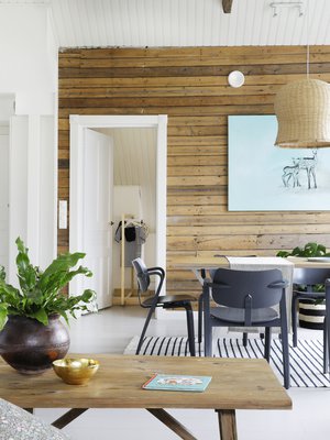 Paljaaksi jätetty lautaseinä tuo lämpöä vaaleaan oleskelutilaan. Ruokapöytä on teetetty huonekaluvalmistaja Tebianilla. Artekin harmaat Aslak-tuolit napakoittavat vaalean sisustuksen. Pöydän päällä on Tikaun bambuvalaisin. Ruokapöydän takana on Hannan hyvän ystävän Manuela Boscon taideteos.